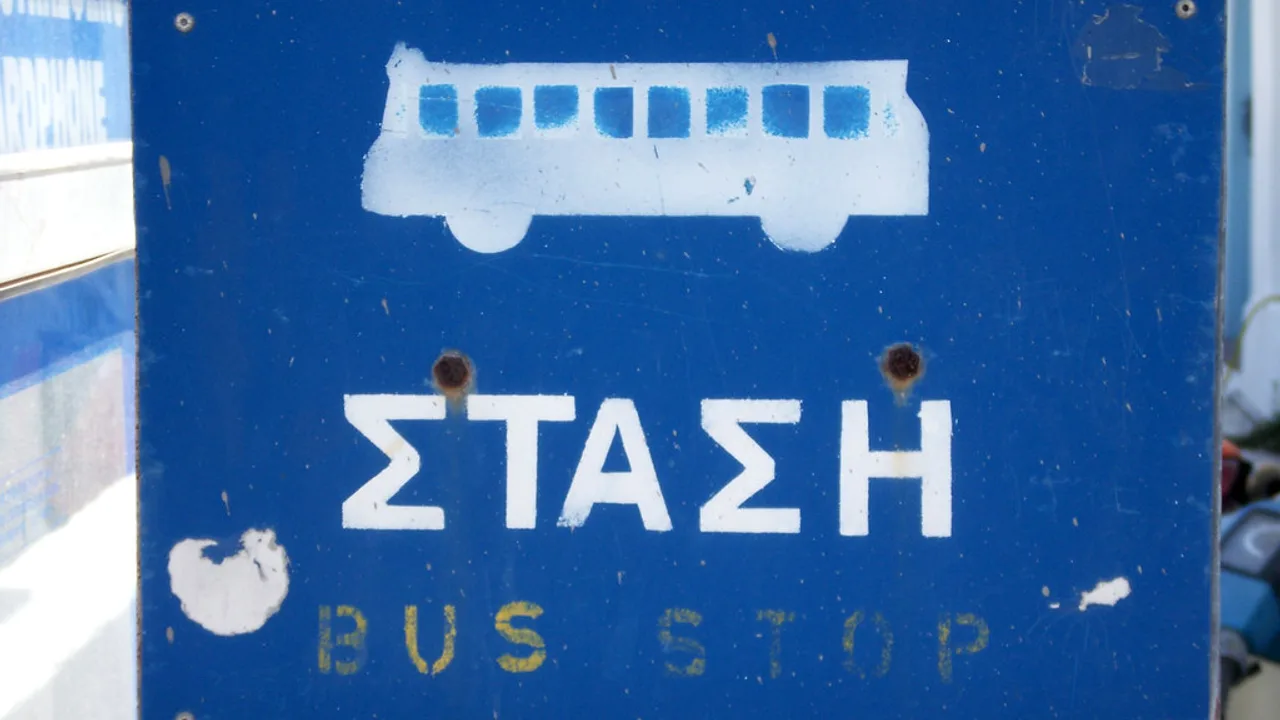 A blue Greek bus-stop sign marked ΣΤΑΣΗ (stop) — Santorini's public buses run from the Fira hub