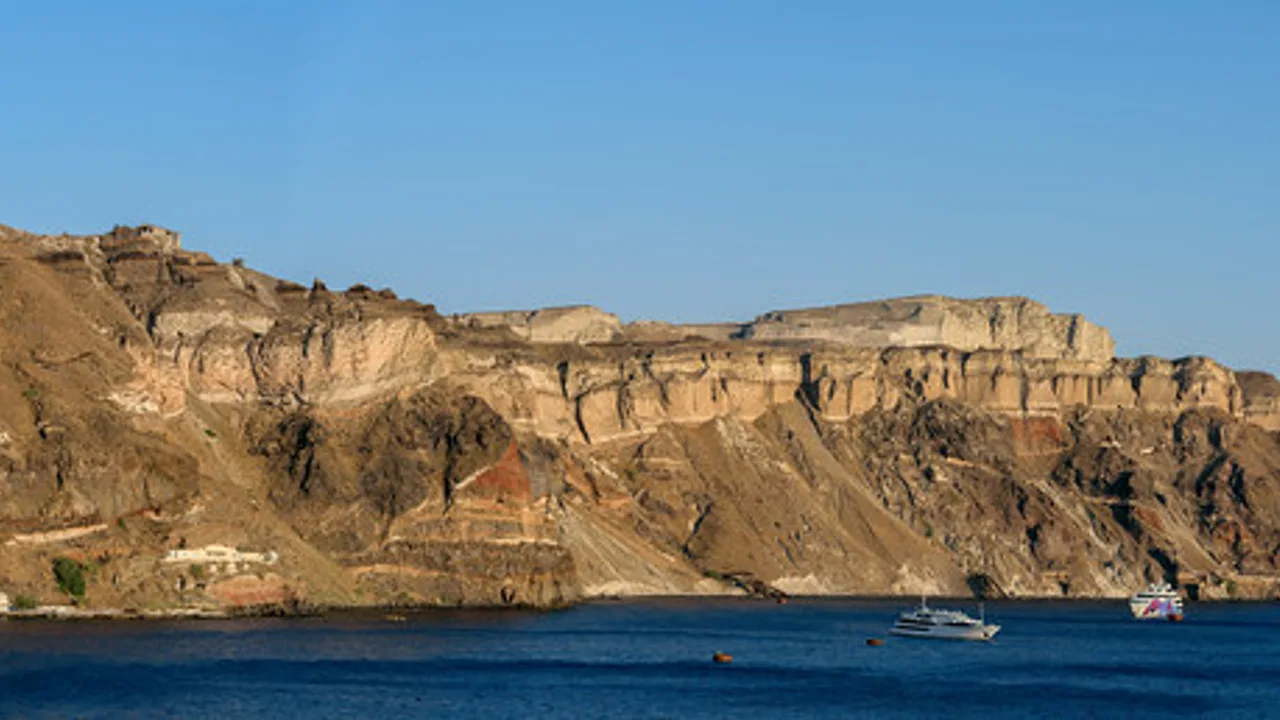 Boats on the water below the volcanic caldera cliffs of Santorini