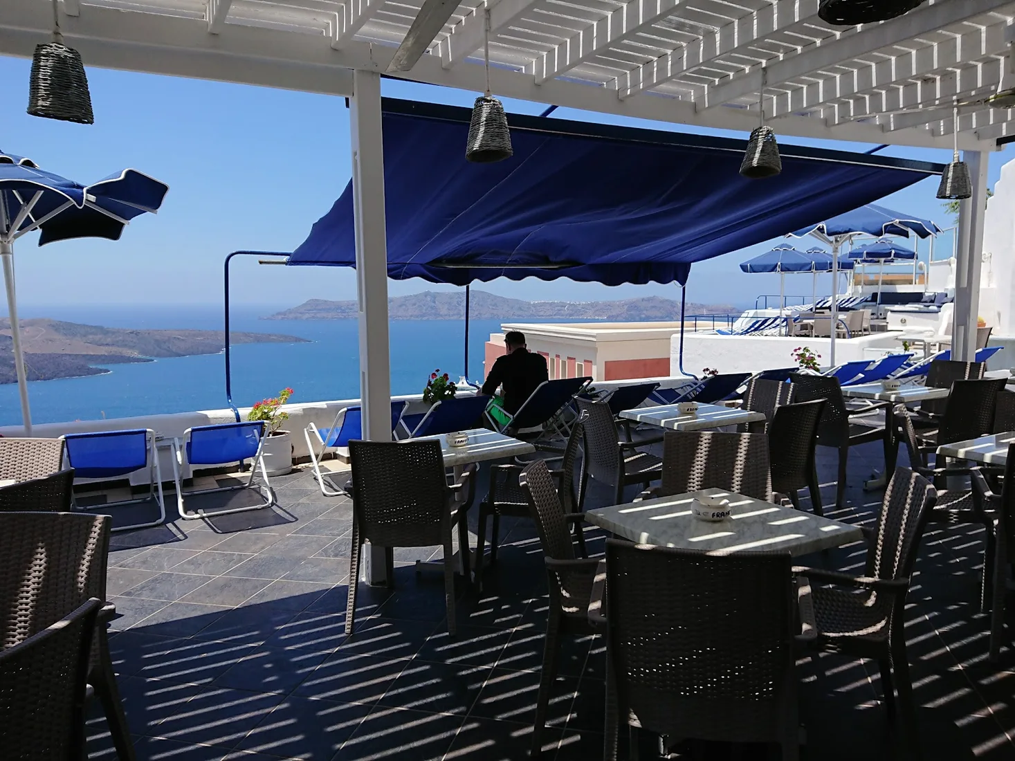 A blue-awning terrace with loungers overlooking the caldera at Franco's Bar, Fira