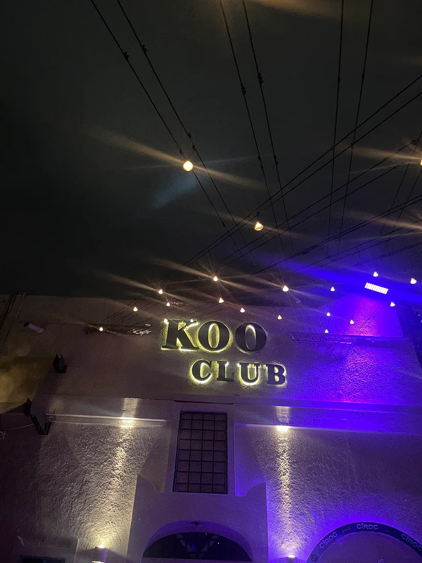 The illuminated 'KOO CLUB' sign under string lights and purple uplighting at Koo Club, Fira