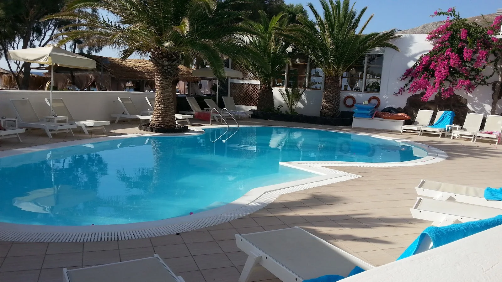 The large curving pool, sun loungers and palms of Aegean Plaza Hotel in Kamari, Santorini