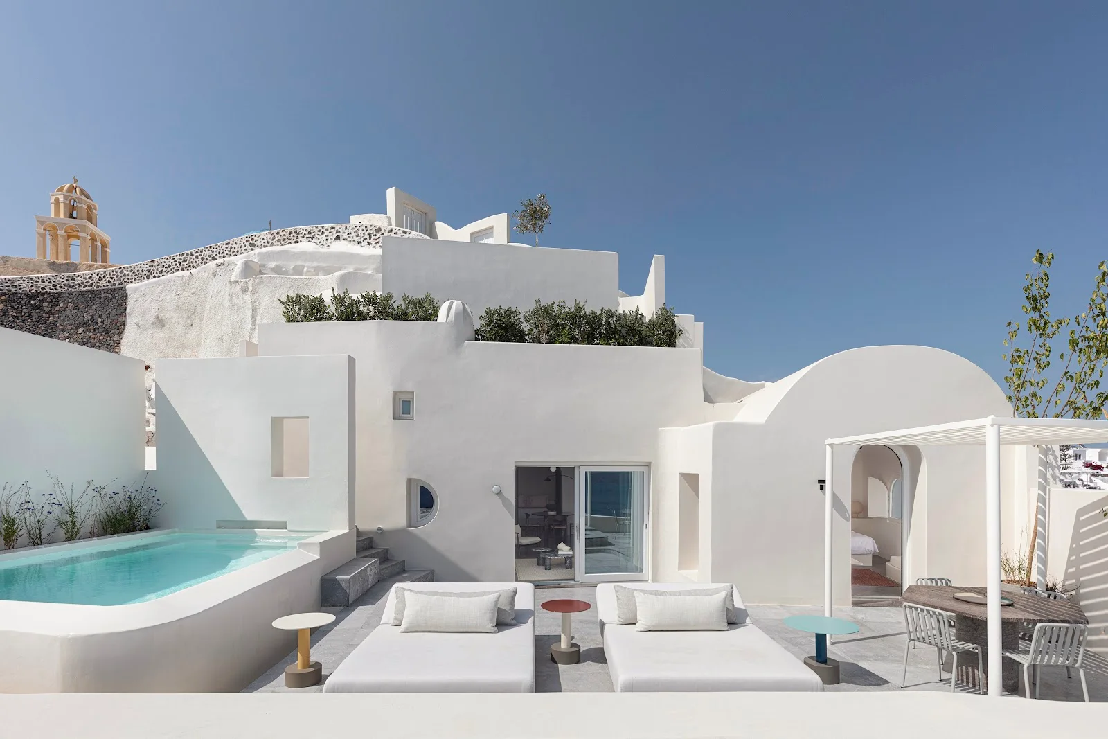 The white terrace, plunge pool and bell tower of Canaves Oia Suites on the caldera cliff in Oia, Santorini