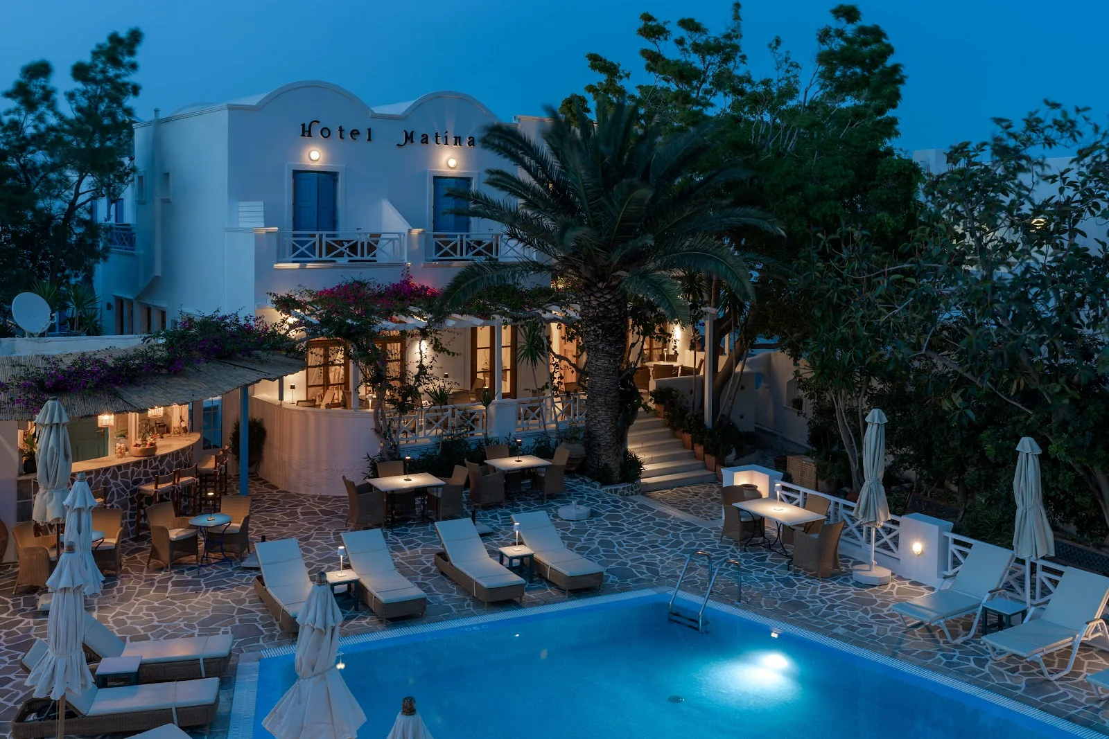 The lit pool, palm and garden terrace of Hotel Matina at dusk in Kamari, Santorini