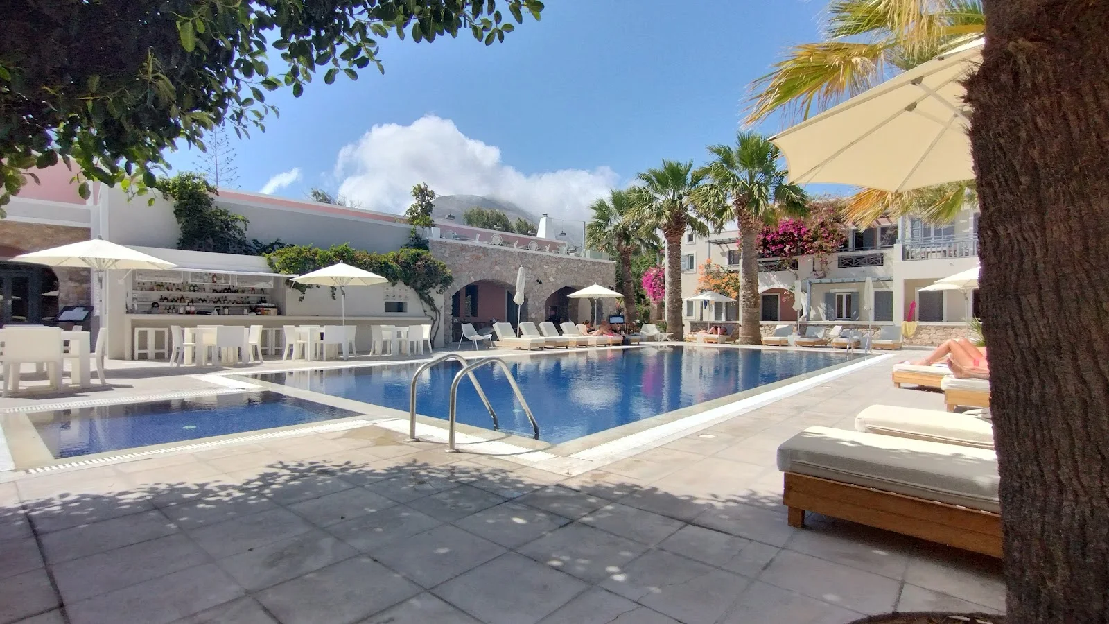 The pool, palms and neoclassical buildings of Rose Bay Hotel below Mesa Vouno in Kamari, Santorini