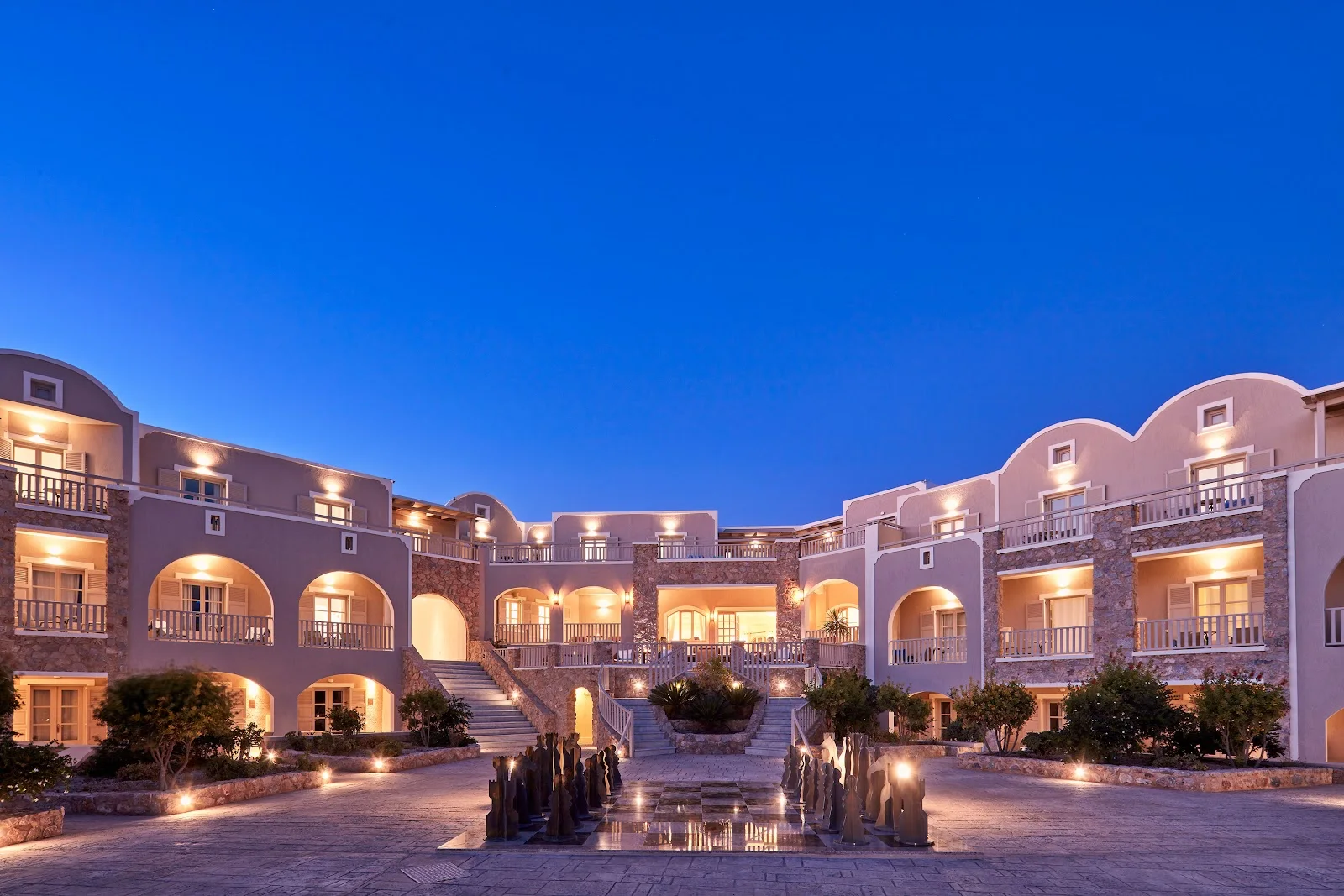 The arcaded courtyard and buildings of Santo Miramare Resort lit at dusk near Perivolos, Santorini