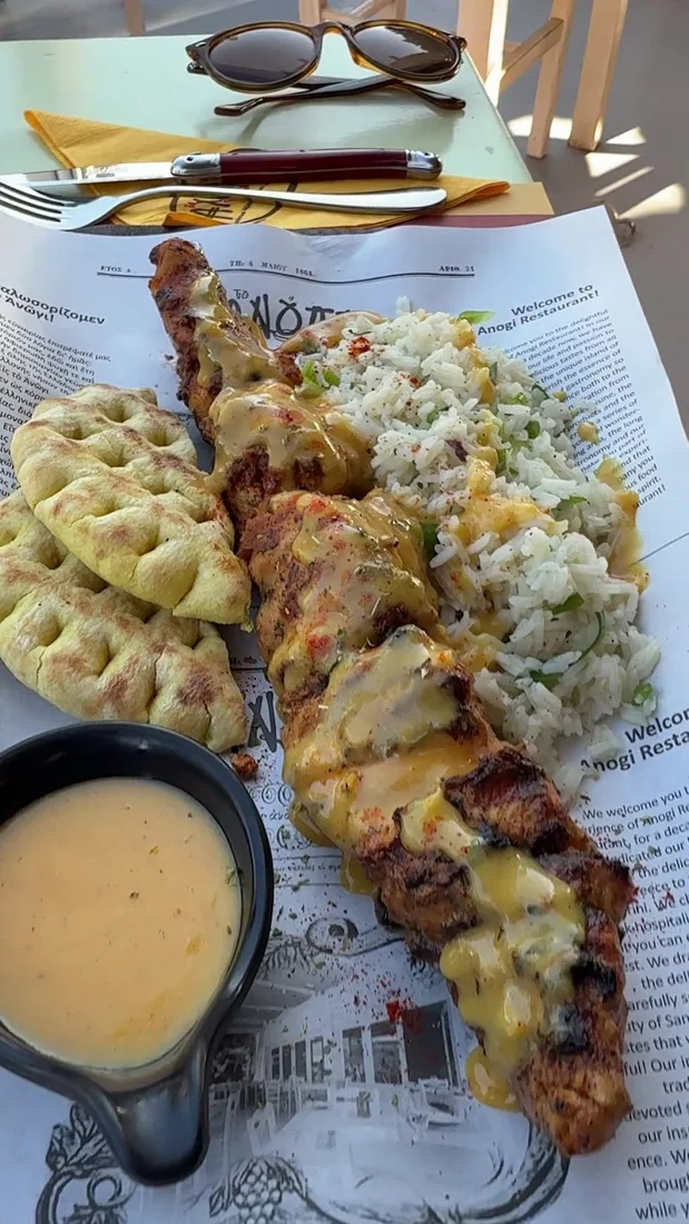 A grilled chicken skewer with rice and pita on an Anogi Restaurant printed placemat, Imerovigli, Santorini