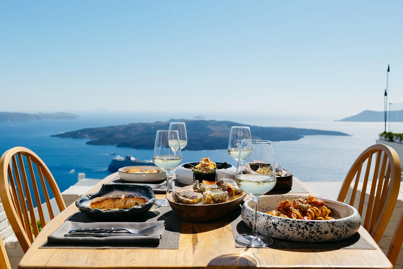 A table of Greek dishes and white wine on the caldera-view terrace at Idol in Fira, Santorini
