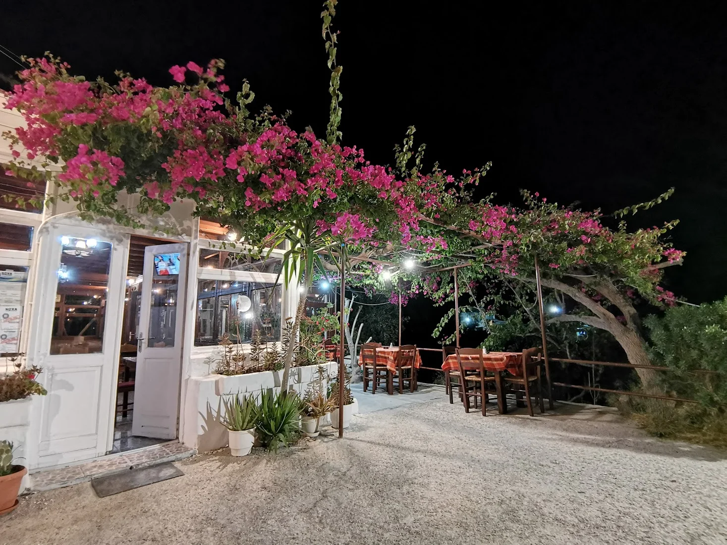 The bougainvillea-draped night exterior of Kritikos Taverna with lit outdoor tables in Messaria, Santorini