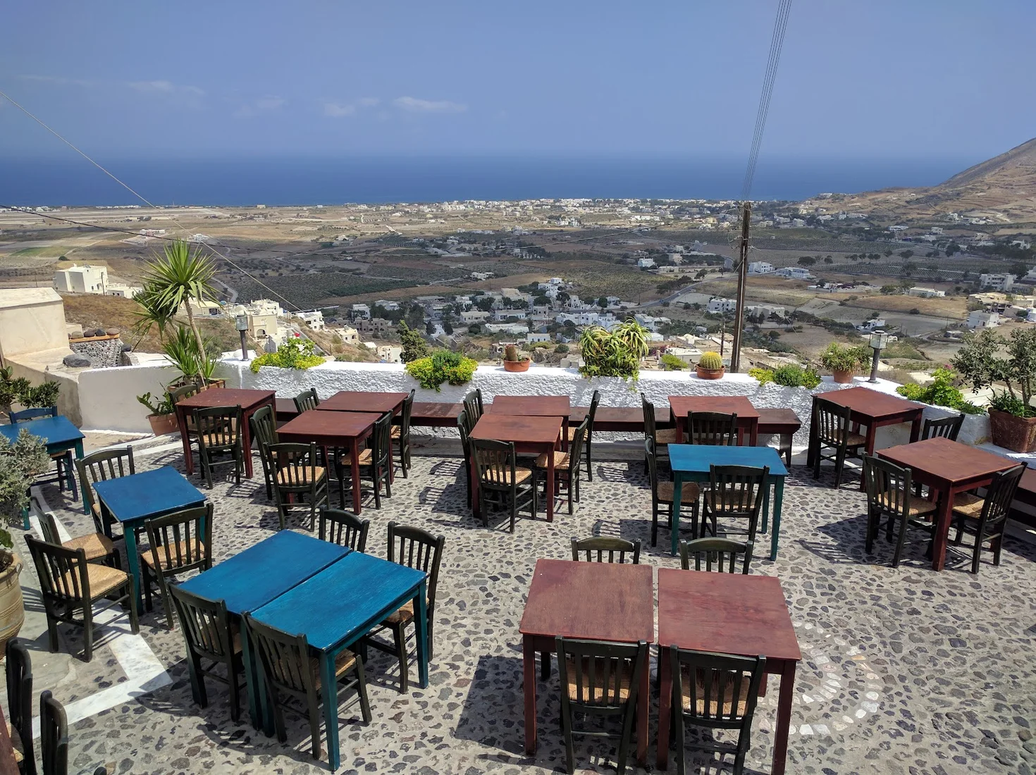 The blue-and-red-tabled terrace of Metaxi Mas looking out over the Santorini plain to the sea, in Exo Gonia