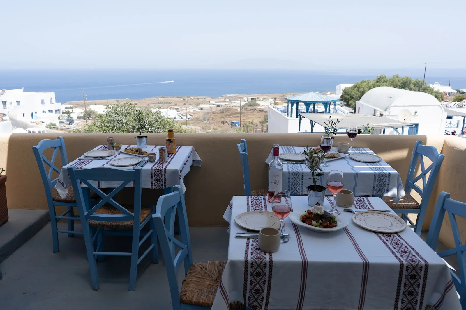 The blue-chaired terrace of Roka restaurant with embroidered tablecloths and a sea view over Oia, Santorini
