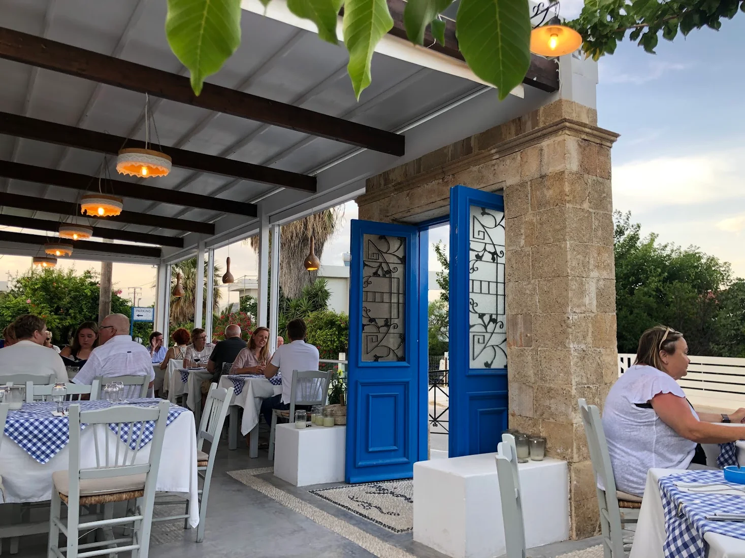 The pergola-shaded terrace with blue doors and white tables at To Psaraki on the marina at Vlychada, Santorini