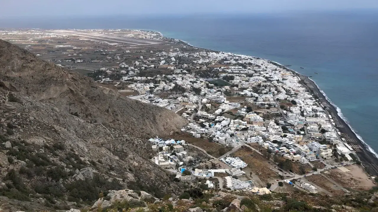 The rugged slope of Mesa Vouno falling away to the black-sand coast and airport far below Ancient Thera, Santorini