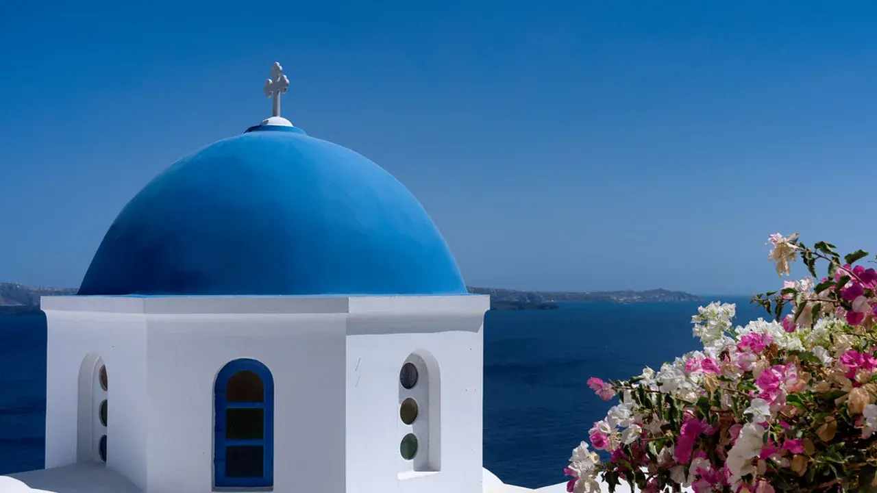A blue-domed church above the Santorini caldera, framed by pink bougainvillea