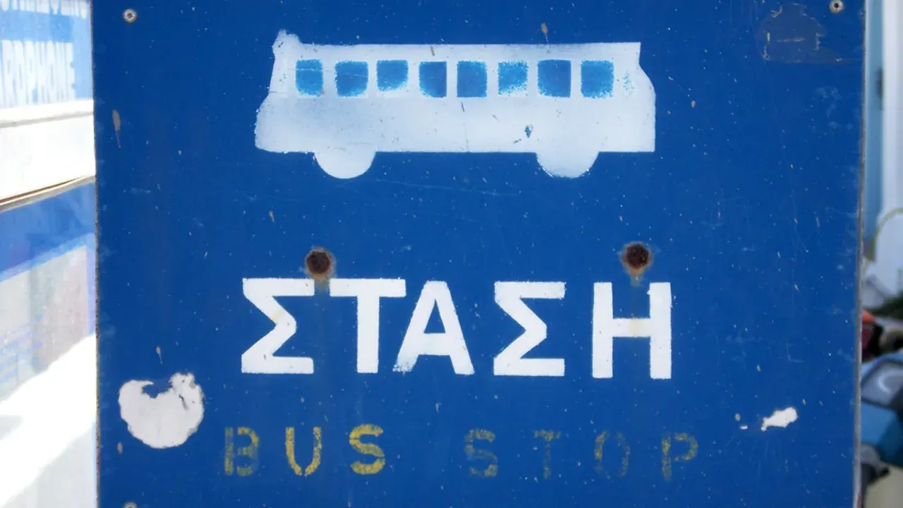 A blue Greek bus-stop sign marked ΣΤΑΣΗ (stop) — Santorini's public buses run from the Fira hub