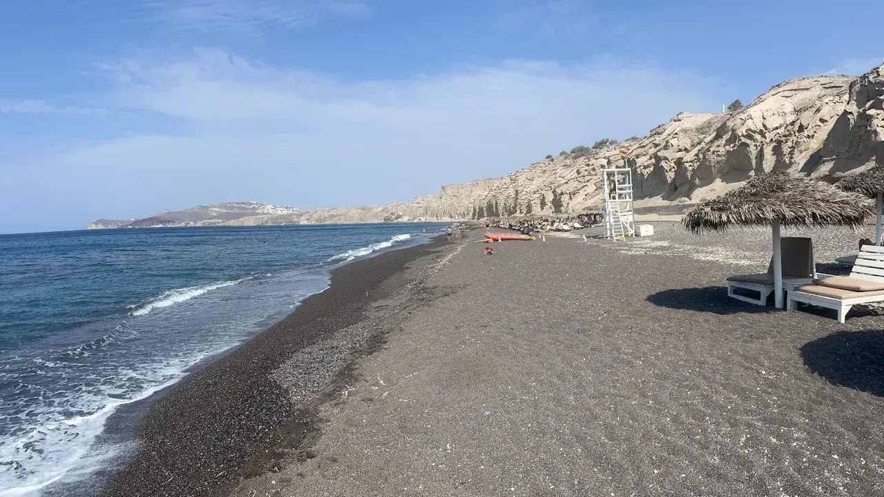 The dark-sand shore of Vlychada beach beneath its pale wind-carved moonscape cliffs, Santorini