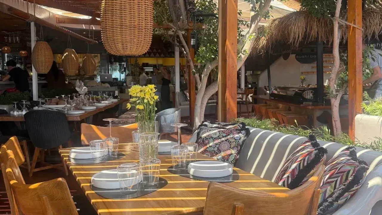 A pergola-shaded dining terrace with set wooden tables at a beach restaurant on Perivolos, Santorini