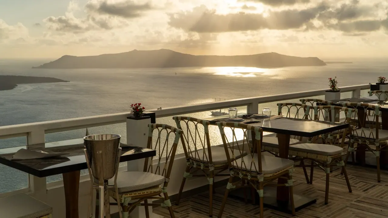 A cliff-edge terrace with rattan chairs looking out to the caldera and volcano at golden hour, Crystal Cocktail Bar, Fira