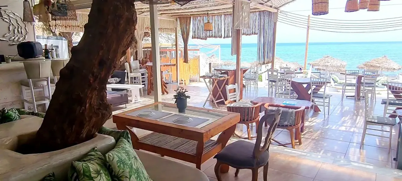 Boho lounge seating under macramé shades with an olive tree and a turquoise sea view at Demilmar, Perivolos