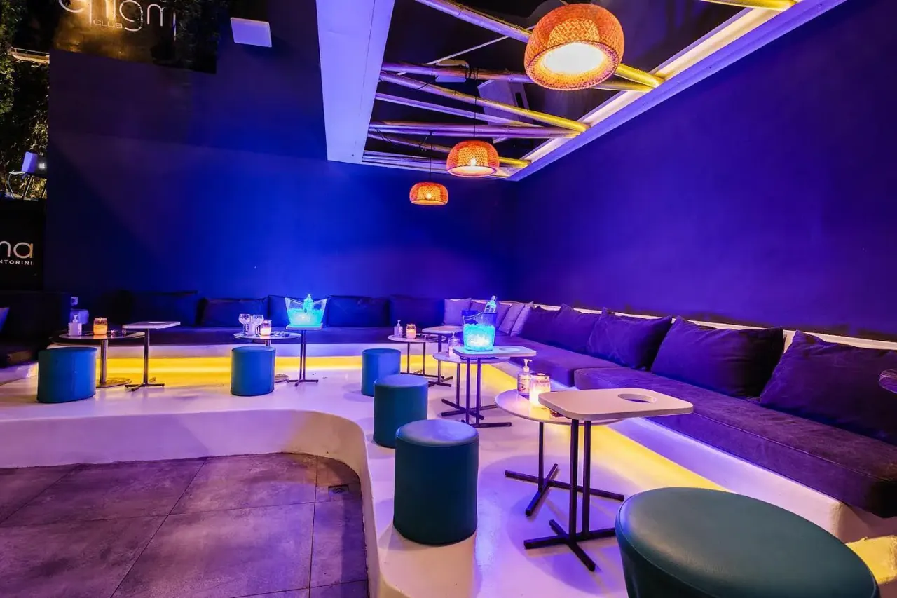The blue velvet banquettes and rattan pendant lights of the open-air lounge at Enigma Club, Fira