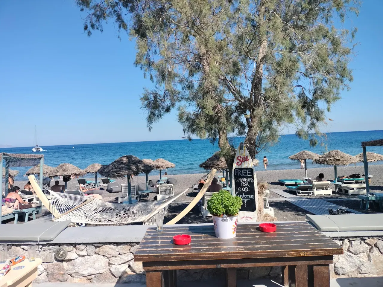 Thatched umbrellas, a hammock and sun-loungers on the black sand at Waves beach bar, Perissa