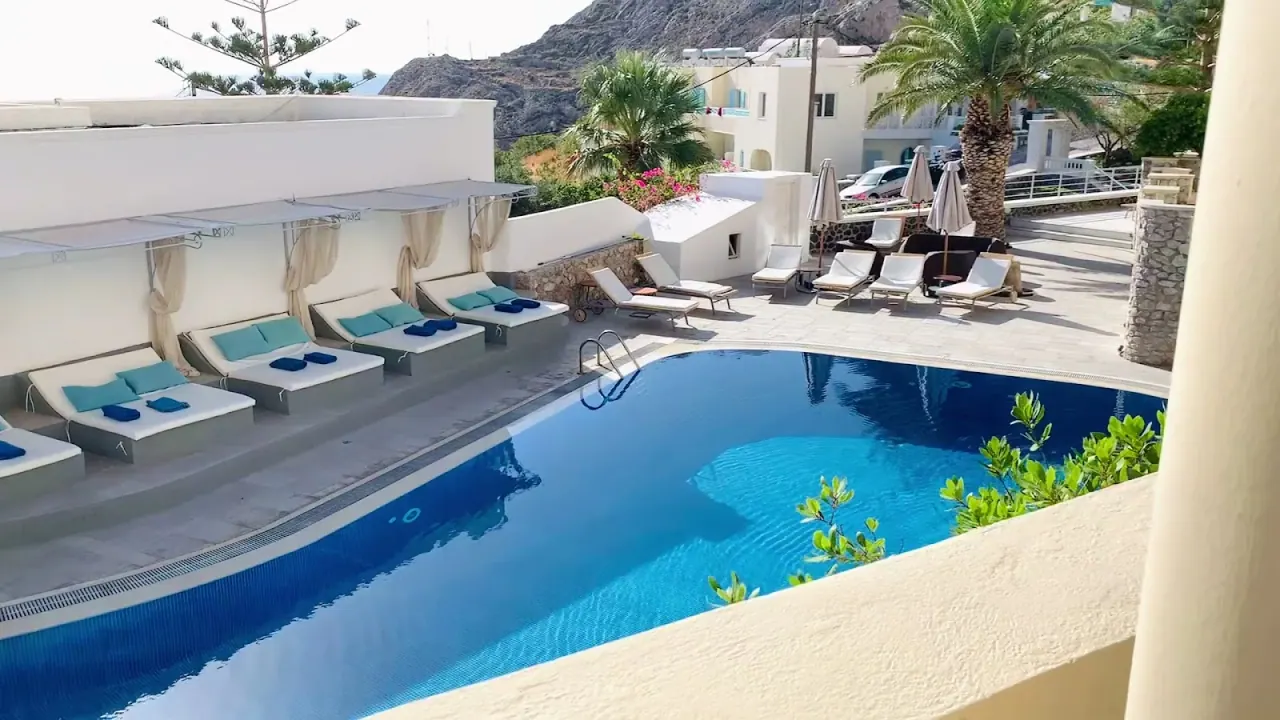 The pool and sun loungers of Antinea Suites below the rock of Mesa Vouno in Perissa, Santorini