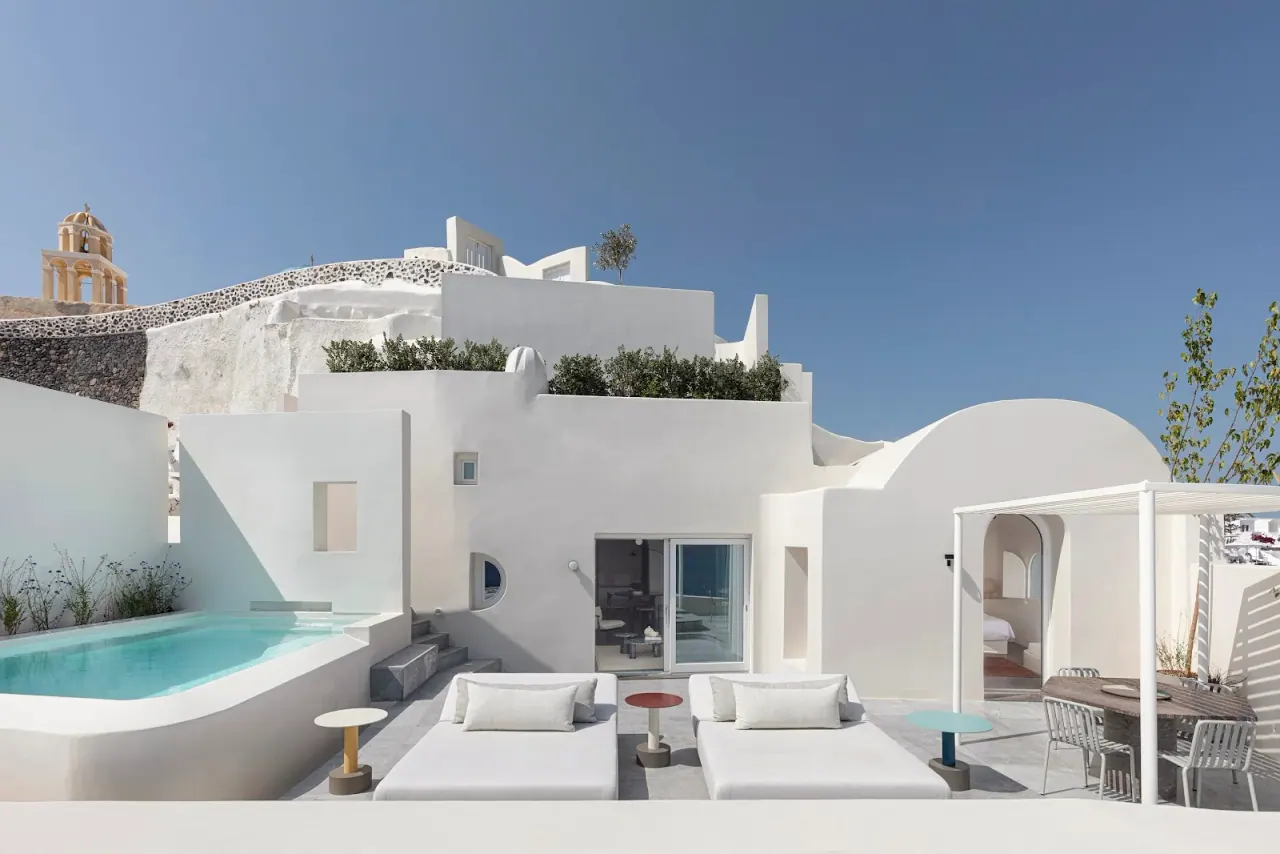 The white terrace, plunge pool and bell tower of Canaves Oia Suites on the caldera cliff in Oia, Santorini