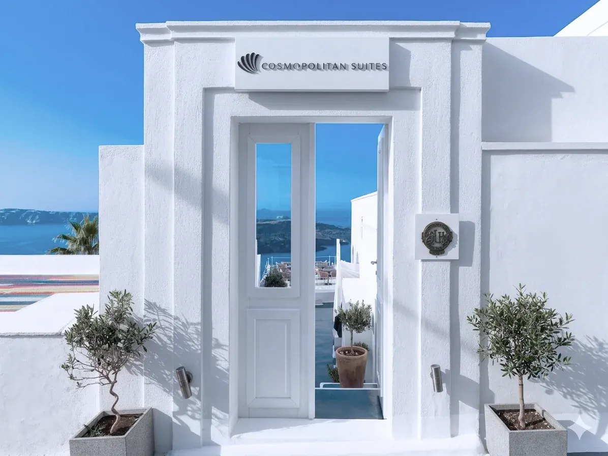 The white entrance of Cosmopolitan Suites with the caldera and sea behind it in Fira, Santorini