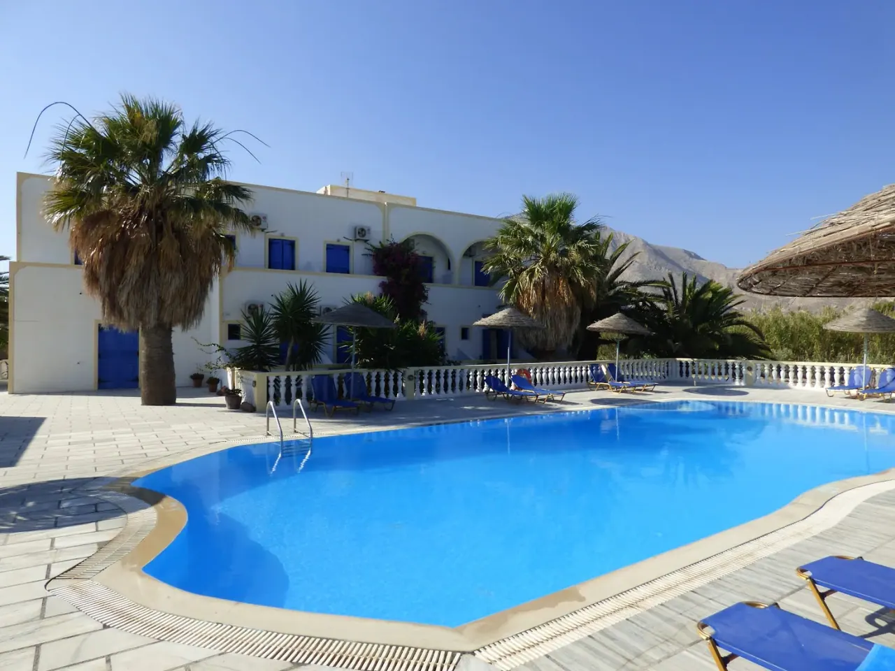The curved pool, sun loungers and whitewashed buildings of Nikolas Villas Aparthotel below Mesa Vouno in Perivolos, Santorini