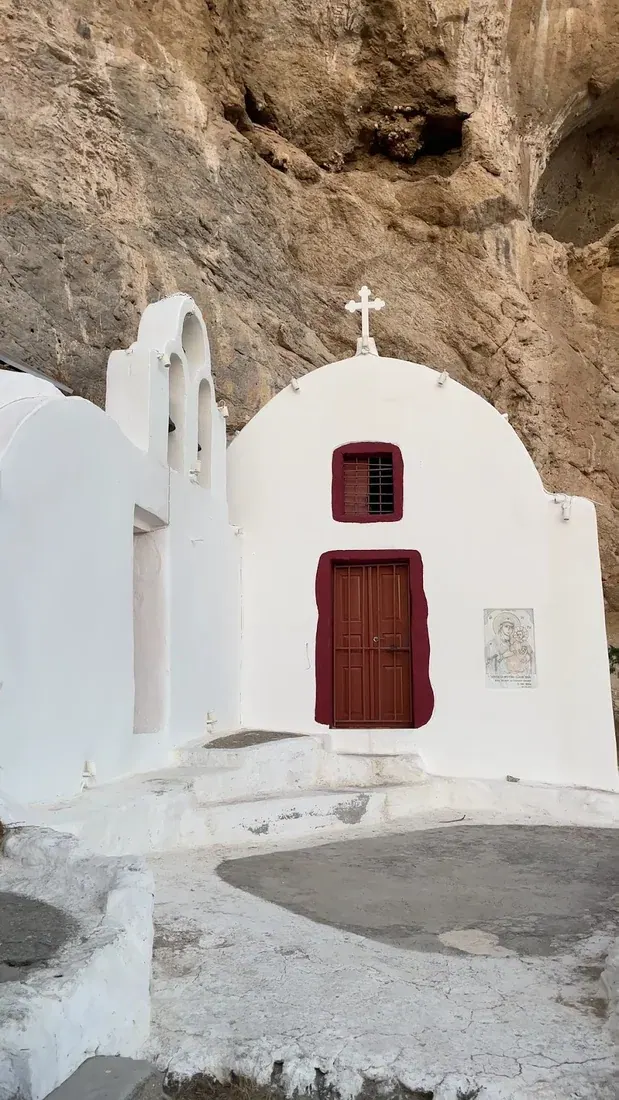 Close view of the Panagia Katefiani chapel with its red door set into the Mesa Vouno rock, Santorini