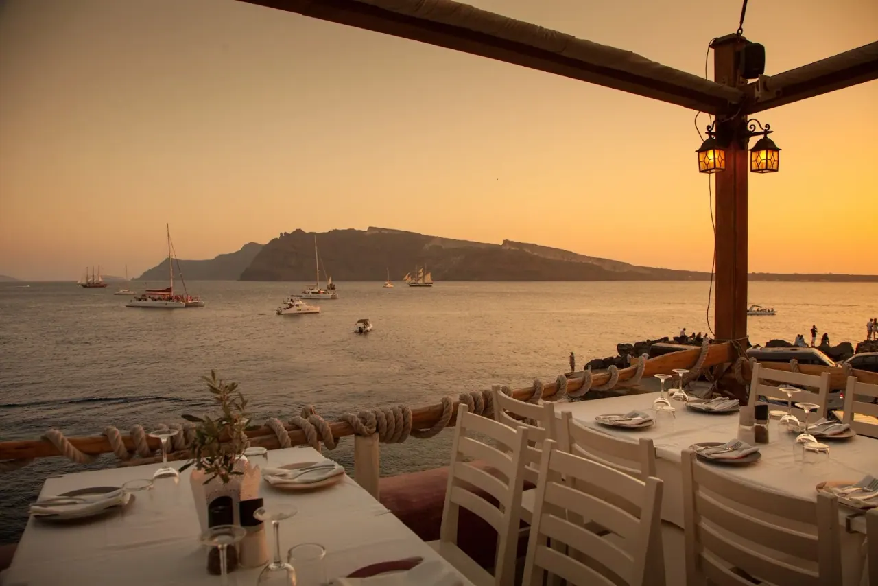Sunset over the caldera and sailing boats from the seafront terrace of Ammoudi Fish Tavern at Ammoudi Bay, Santorini
