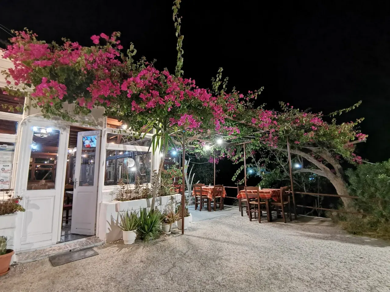 The bougainvillea-draped night exterior of Kritikos Taverna with lit outdoor tables in Messaria, Santorini