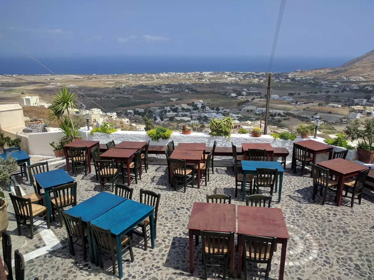 The blue-and-red-tabled terrace of Metaxi Mas looking out over the Santorini plain to the sea, in Exo Gonia