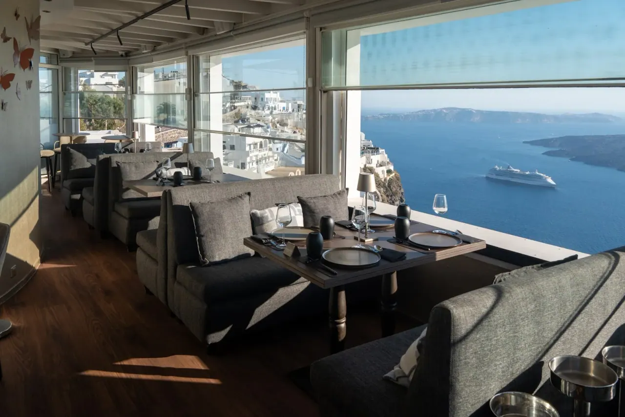 The caldera-view lounge and terrace with a cruise ship on the water at Mylos in Firostefani, Santorini
