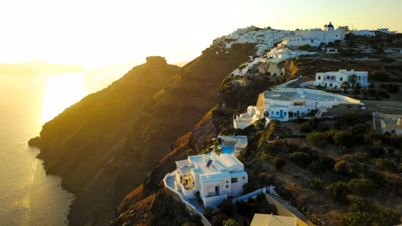 White clifftop villas and infinity pools above the Santorini caldera at golden hour