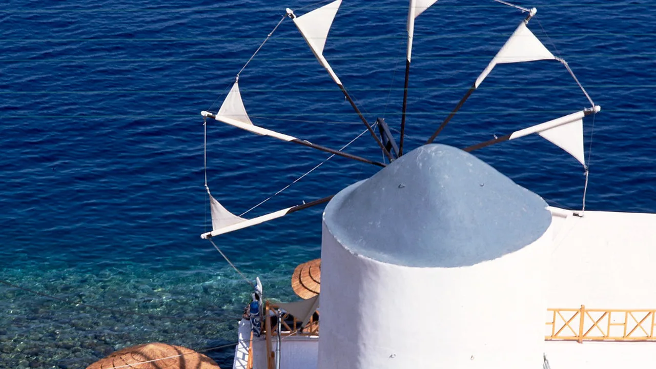 A whitewashed Greek-island windmill with cloth sails above the deep-blue Aegean