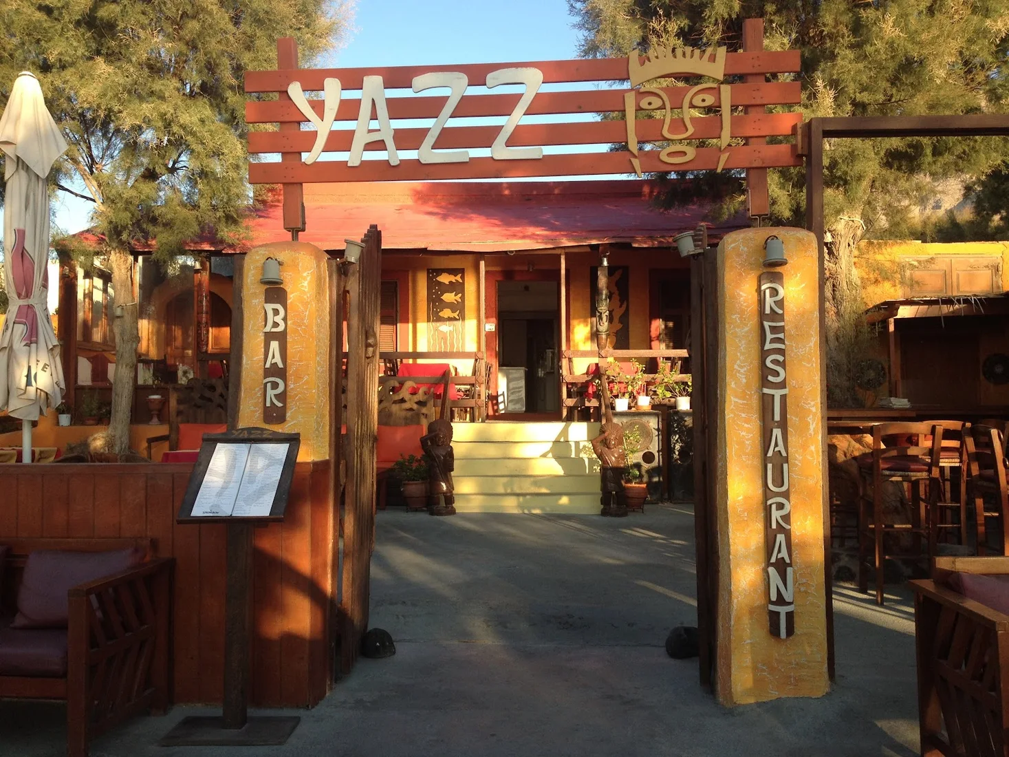 The carved-wood 'YAZZ' sign over the lantern-lit courtyard entrance at Yazz bar, Perissa