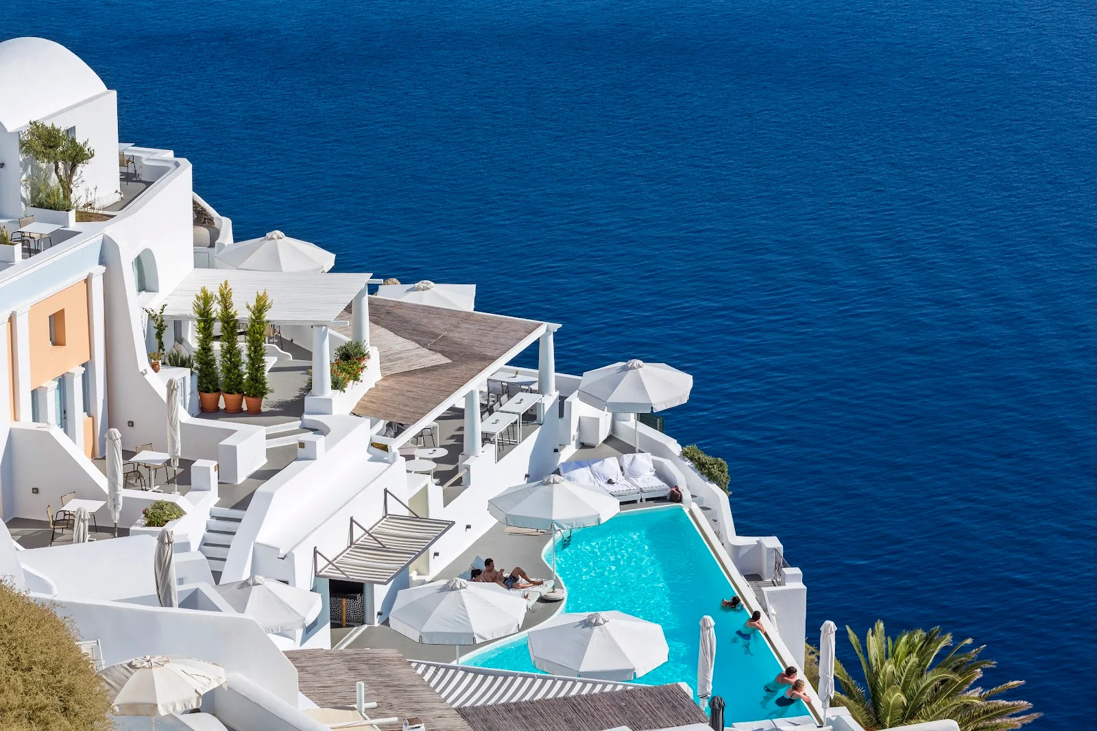 The white cliffside buildings and infinity pool of Katikies Santorini above the deep-blue caldera in Oia