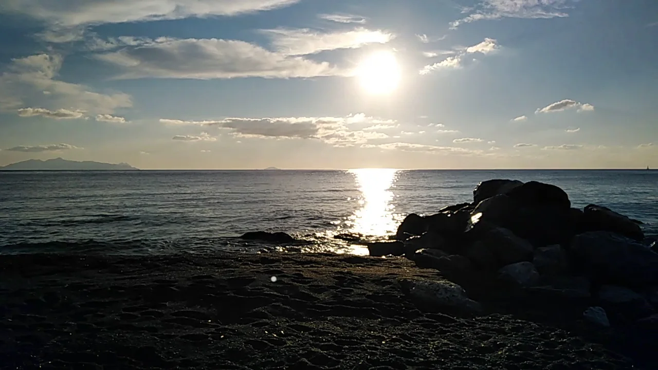Sunset over the sea and volcanic rocks at the edge of Perissa Beach, Santorini