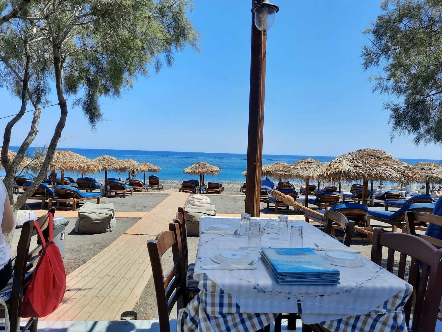 Beachfront tables under thatched umbrellas looking out to the black sand and sea at Fish Tavern o Perivolos, Santorini