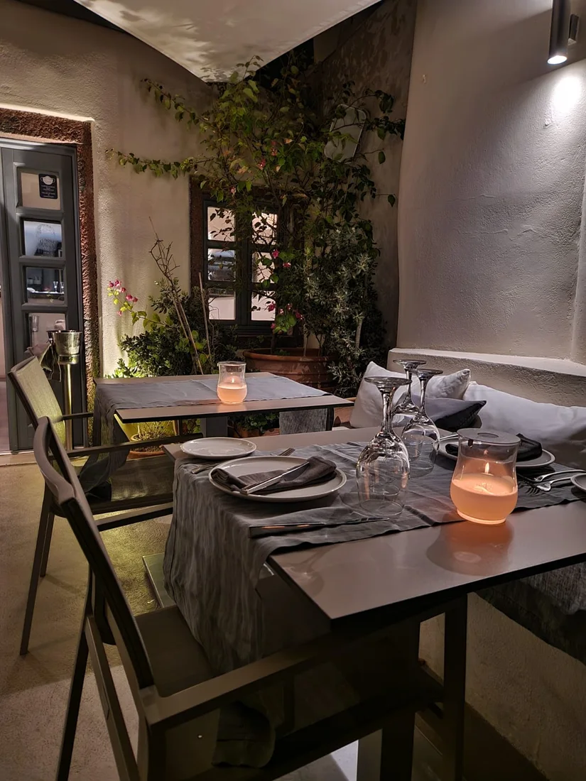 A candlelit terrace table set at dusk with plants and grey linens at Kapari Wine Restaurant in Imerovigli, Santorini