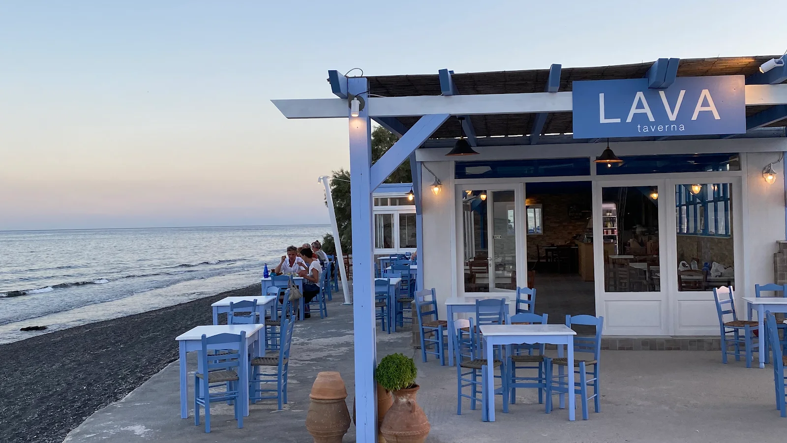 The blue-and-white beachfront terrace of Lava Taverna on the black sand near Perivolos, Santorini