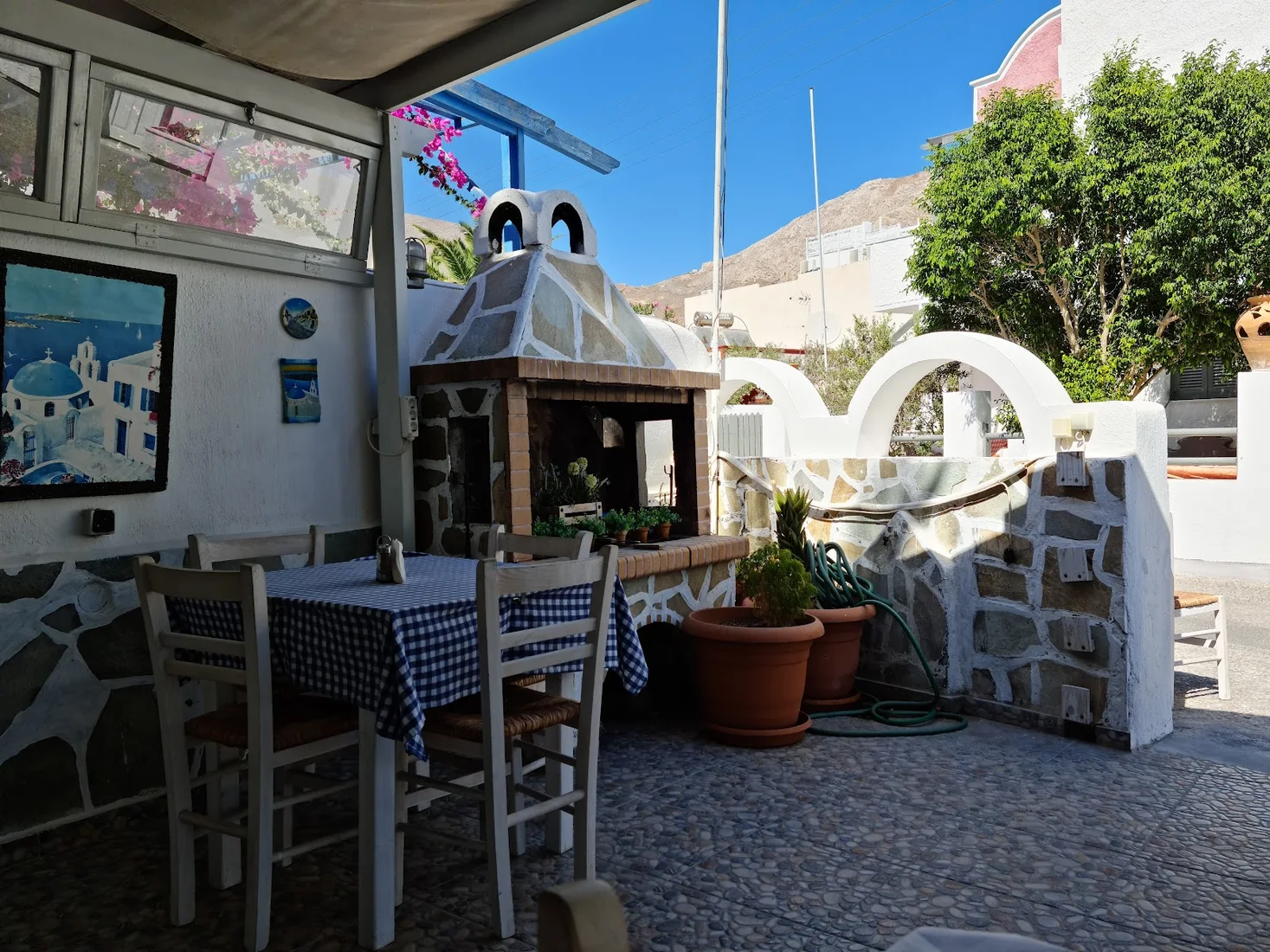 The stone-walled courtyard of Mama's Food taverna with a wood oven, blue-checked tablecloths and bougainvillea in Perissa, Santorini